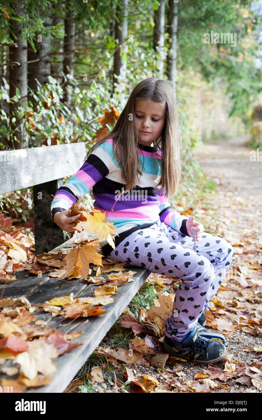 Mädchen sitzen auf einer Holzbank beim Sammeln von Laub im Herbst