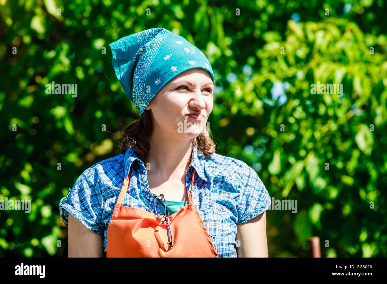Reife lustige Bäuerin Kopftuch Schürze Hut im Garten Stockfotografie